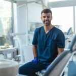 A smiling dentist in scrubs sitting in an operatory