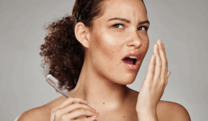 A woman holding a tooth brush tries to determine if she has bad breath.