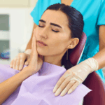 A young girl sits in a dentist chair with her hand on her cheek, indicating pain from a wisdom tooth.