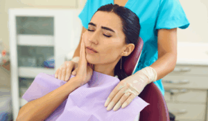 A young girl sits in a dentist chair with her hand on her cheek, indicating pain from a wisdom tooth.