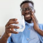 Smiling man with blue shirt and glasses holding a glass of water