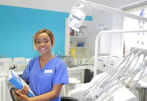 A young, smiling staff member in a dental exam room ready to help their boss