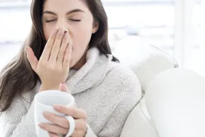 A woman with sleep apnea yawning and holding a full coffee cup